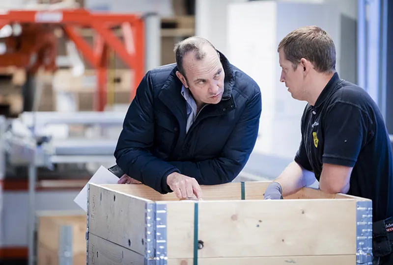 To menn i samtale over en trekasse i verkstedet