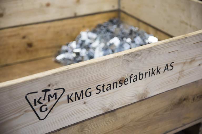 Trekasse merket KMG Stansefabrikk AS, fylt med stansede stålklips